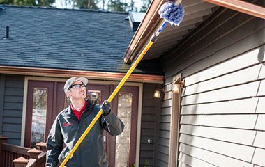 Eastside Exterminator cleaning the gutters of someone's house with a large tool. 