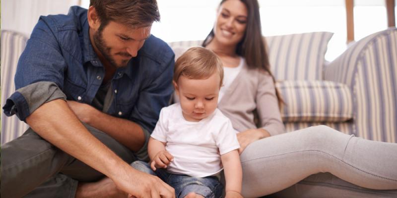 Father, mother, and baby sitting on the floor of their home playing with blocks.