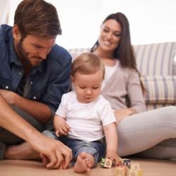 Father, mother, and baby sitting on the floor of their home playing with blocks.